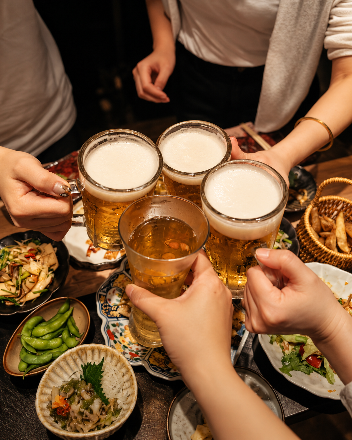 几只啤酒杯在餐桌上碰杯，周围摆着菜品